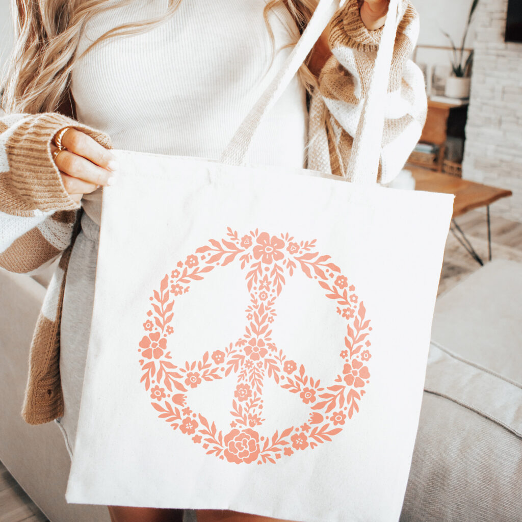 Woman holding a white tote bag with a floral peace sign on it.